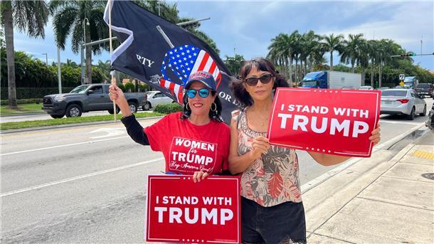 Zwei Trump-Anhängerinnen empfangen den Ex-Präsidenten vor seinem Hotel in Miami mit Schildern, auf denen „Ich stehe hinter Trump“ geschrieben steht.