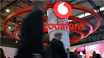 Menschen gehen an einem großen Vodafone-Aufsteller vorbei.